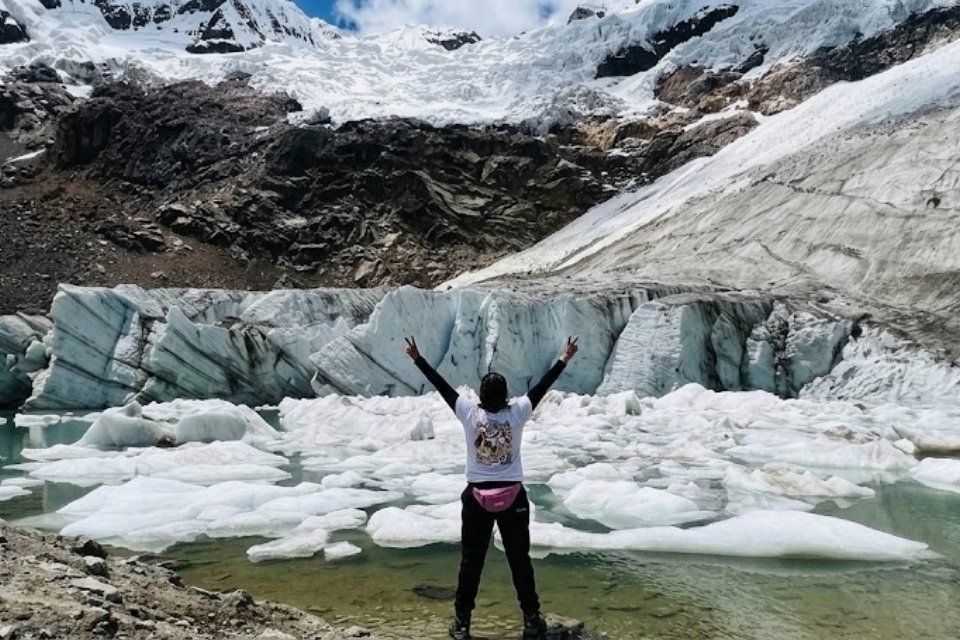 A close-up view of a traveler with Andeando Peru observing floating icebergs in the turquoise waters of Laguna Congelada, with the massive glacier of Nevado Copa in the background, showcasing the uncrowded and accessible high-altitude beauty of the Rocotuyoc circuit in Huaraz.