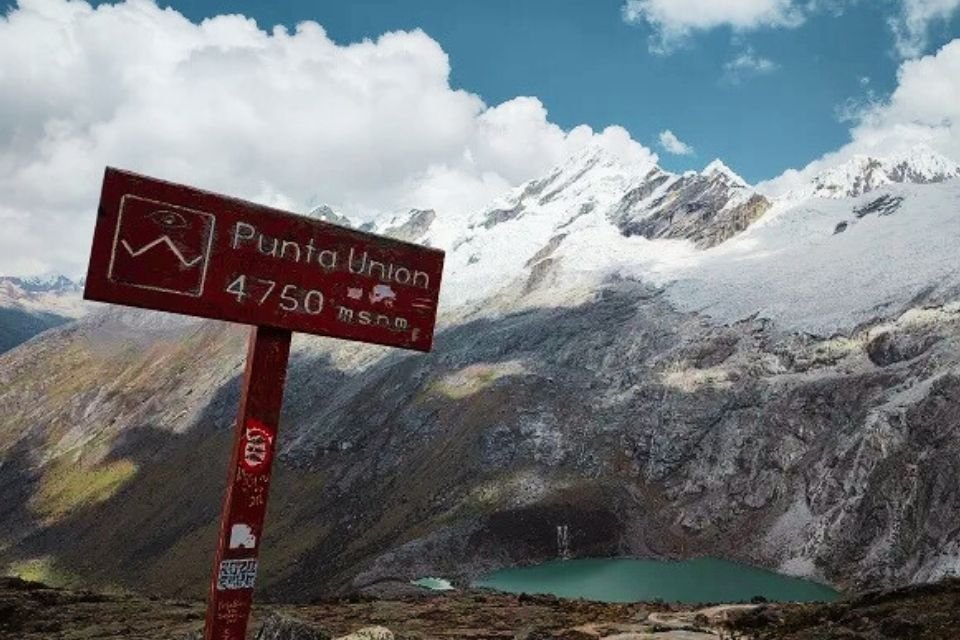 Rustic wooden sign at Punta Union Pass marking 4,750 masl (15,584 ft) with a breathtaking view of a turquoise glacial lagoon and the snow-capped peaks of the Cordillera Blanca by Andeando Perú