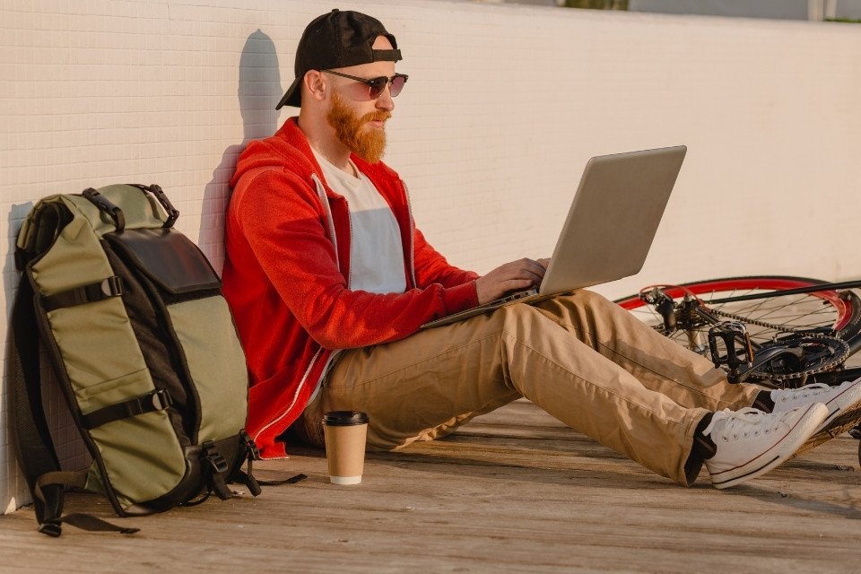 digital nomad with a red hoodie and a green trekking backpack using a laptop outdoors in huaraz to book an andean adventure tour with andeando peru
