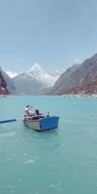 Tourist enjoying a boat ride on the turquoise waters of Paron Lake, surrounded by the majestic peaks of the Cordillera Blanca near Huaraz, Peru.